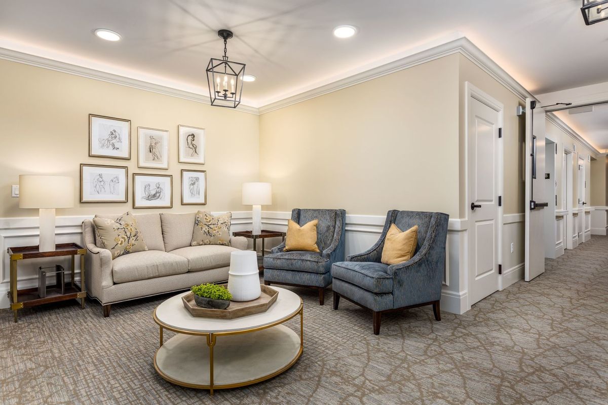 A cozy living room with a comfortable sofa, two blue armchairs, a round coffee table, and decorative artwork on the wall.