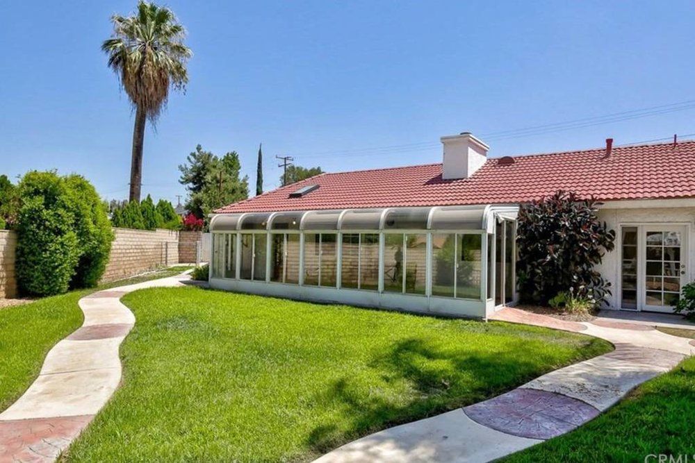 A backyard view of a house with a sunroom and green lawn under a clear blue sky.