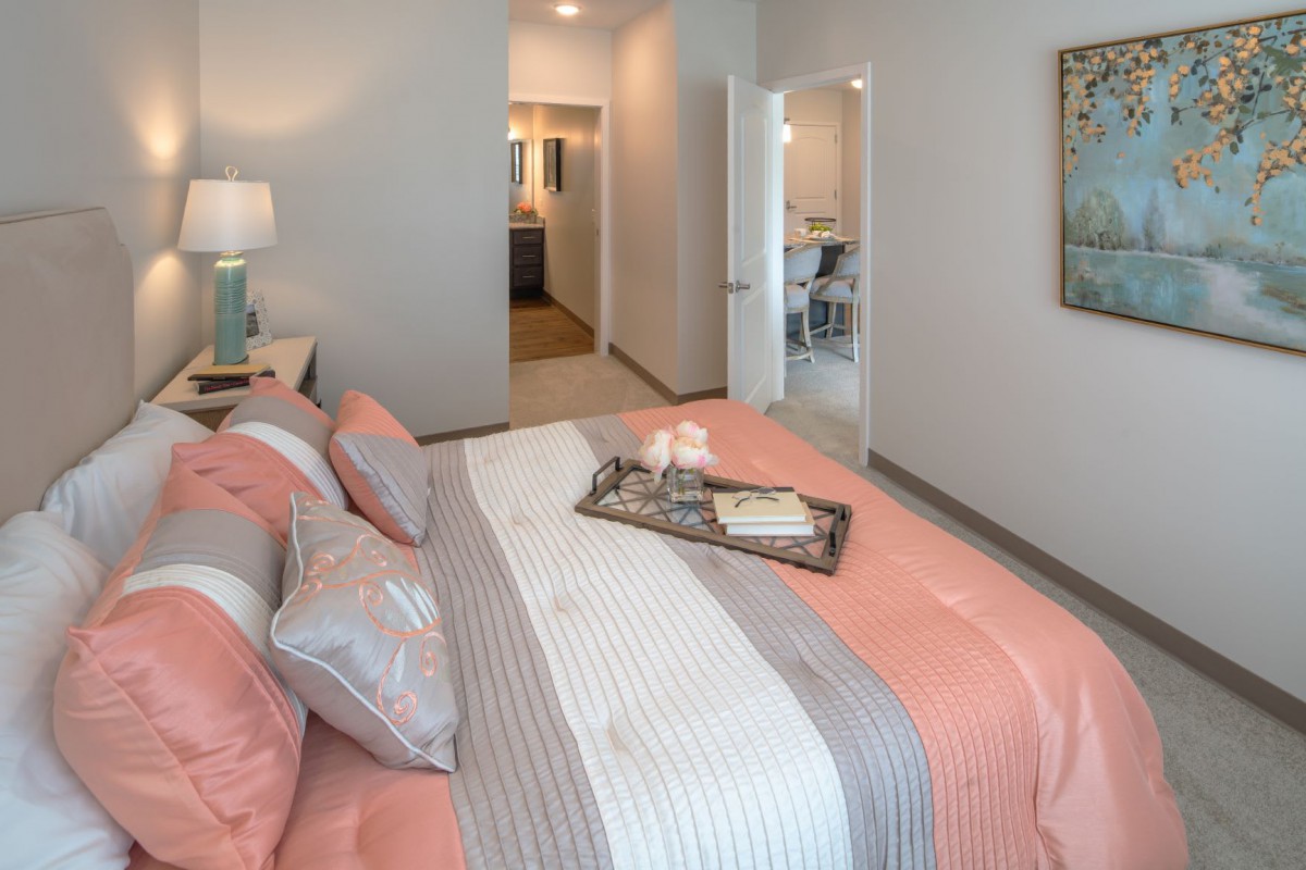 A modern bedroom featuring a neatly made bed with pastel-colored bedding, a decorative tray, and a lamp on the nightstand.