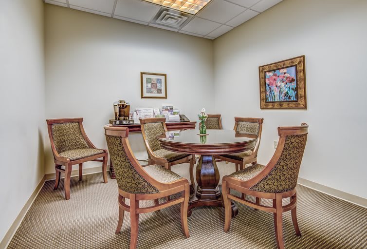 A small meeting room with a round table surrounded by chairs, decorated with artwork and simple furnishings.
