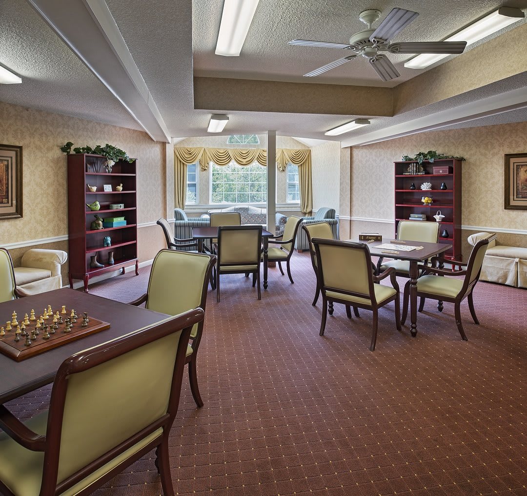 A well-lit room with tables and chairs, featuring bookshelves and a chessboard.
