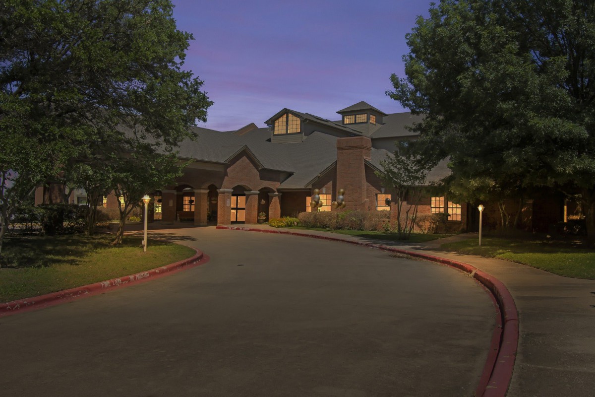 A well-lit building with a driveway at dusk.