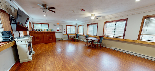 A spacious dining area featuring wooden floors, natural light from multiple windows, and cozy furniture arrangements.