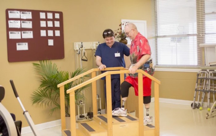 A patient with a prosthetic leg receives assistance during rehabilitation in a healthcare facility.