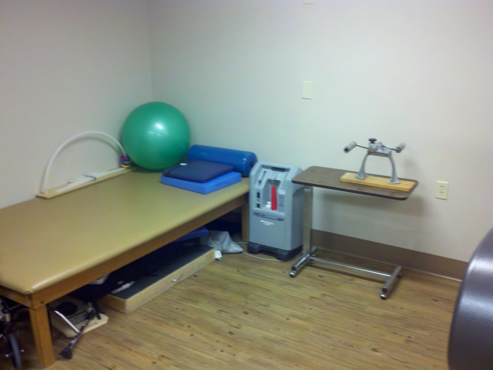 A physical therapy room equipped with a therapy ball, treatment bed, and exercise equipment.
