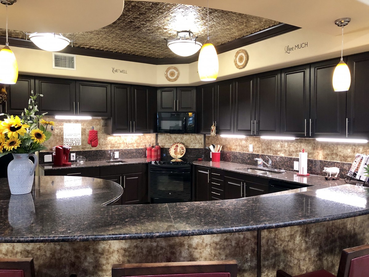 A modern kitchen with dark cabinets and granite countertops, featuring stylish pendant lighting and a decorative backsplash.