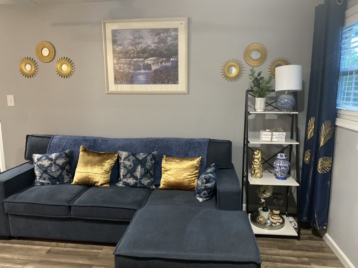 A stylish living room featuring a dark sofa with patterned and gold cushions, complemented by wall art and decorative shelving.