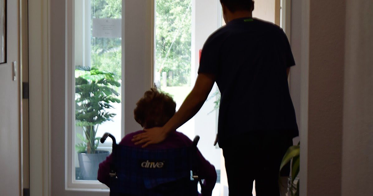 A caregiver assisting a person in a wheelchair indoors.
