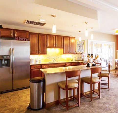A modern kitchen with wooden cabinets, stainless steel appliances, and bar seating.