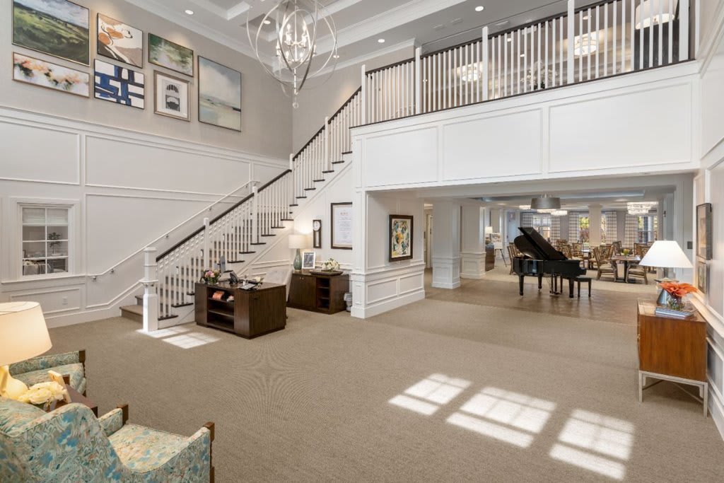 A spacious and elegantly designed lobby with a grand staircase, chandelier, and a piano.