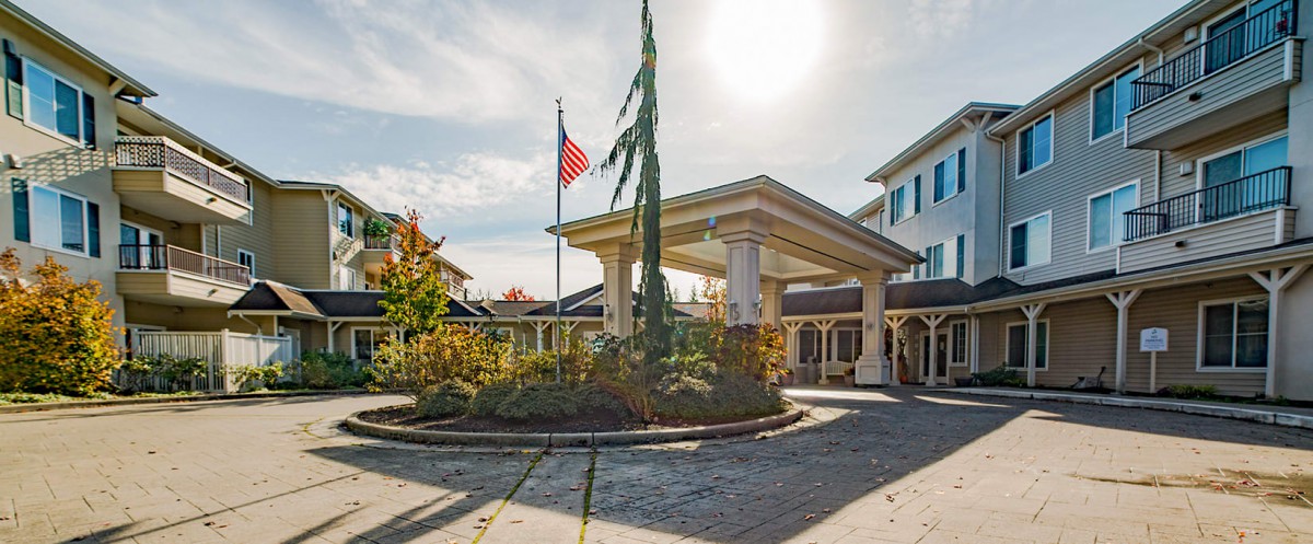 A building entrance with an American flag and landscaped roundabout on a sunny day.