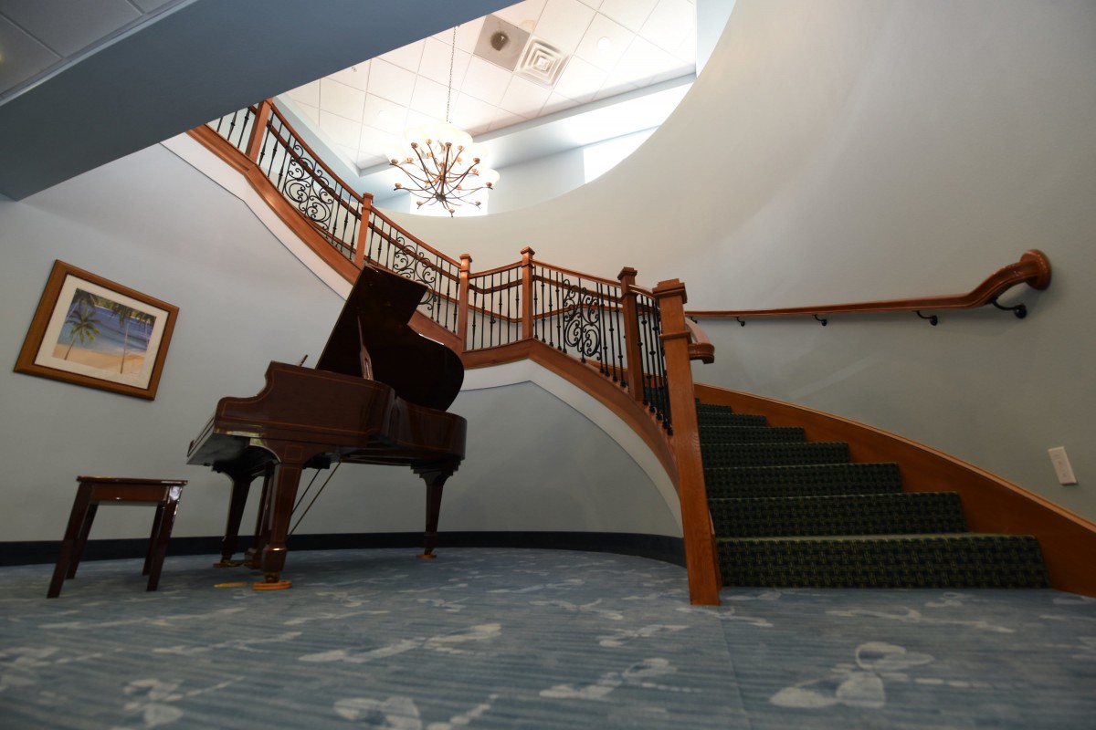 A grand piano sits elegantly at the base of a sweeping staircase in a beautifully designed interior.