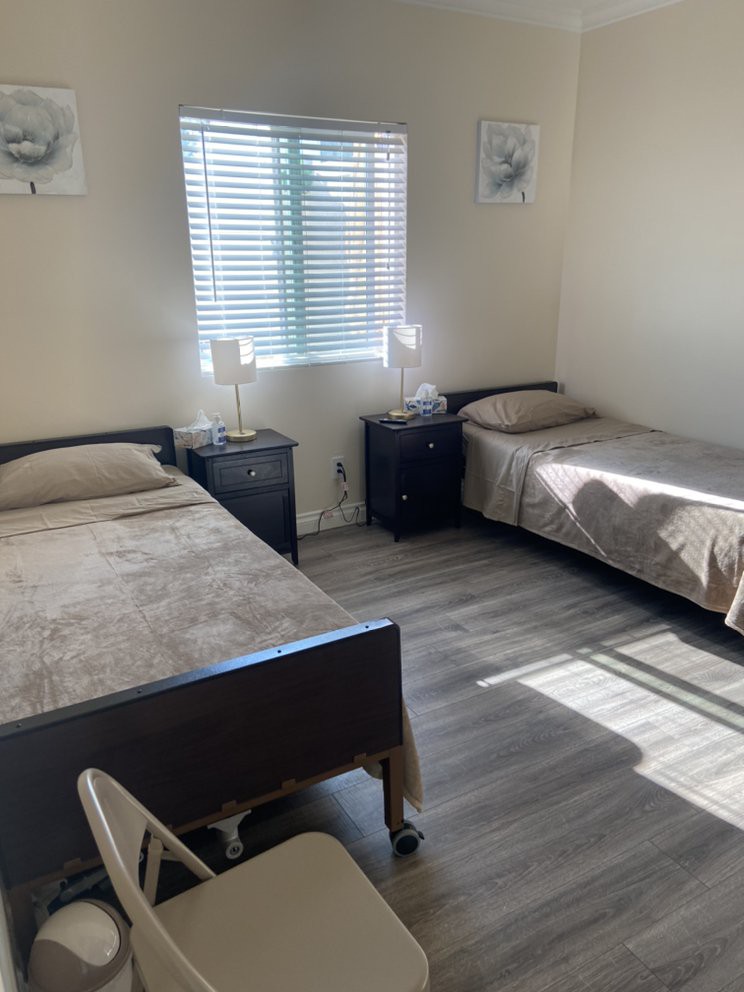 A minimalist bedroom featuring two twin beds, nightstands with lamps, and sunlight streaming through the window.