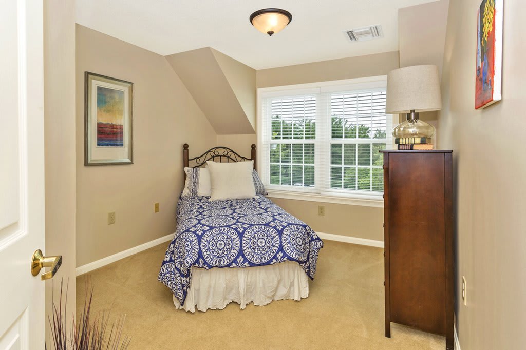 A cozy bedroom with a single bed, blue patterned bedding, a large window, and neutral-colored walls.