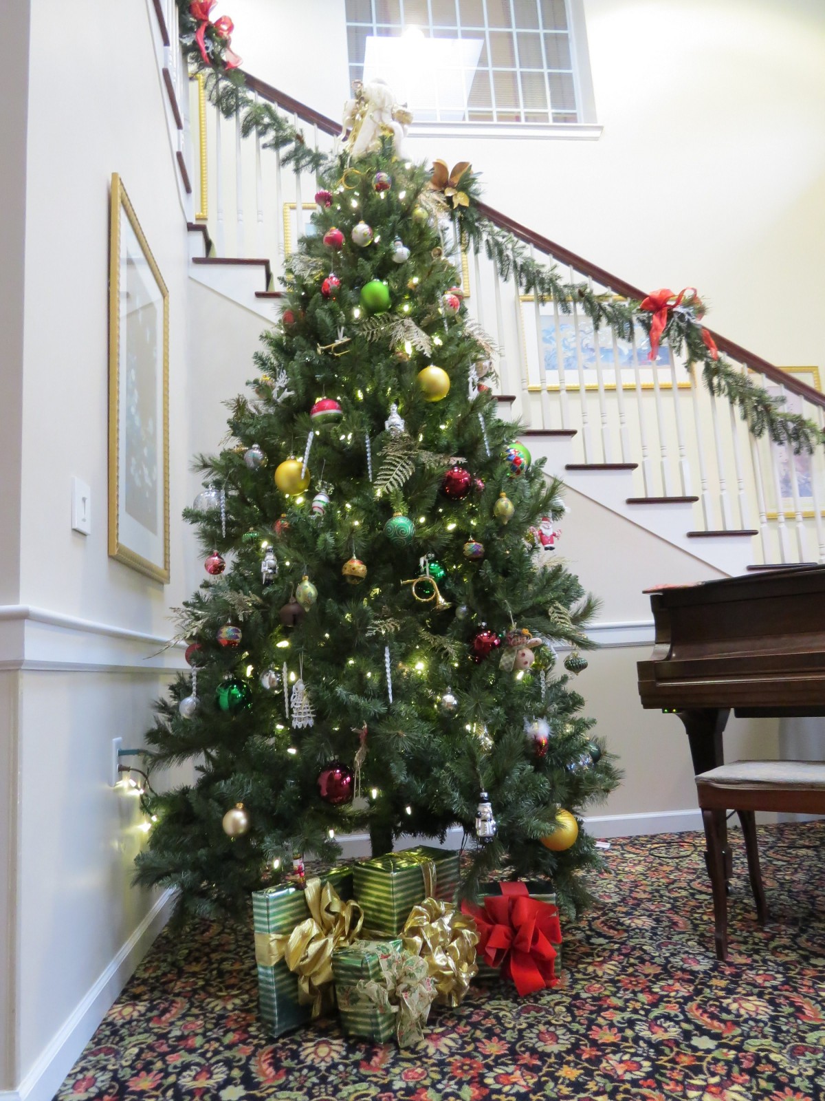 A beautifully decorated Christmas tree stands near a staircase, adorned with colorful ornaments and surrounded by festive decorations.
