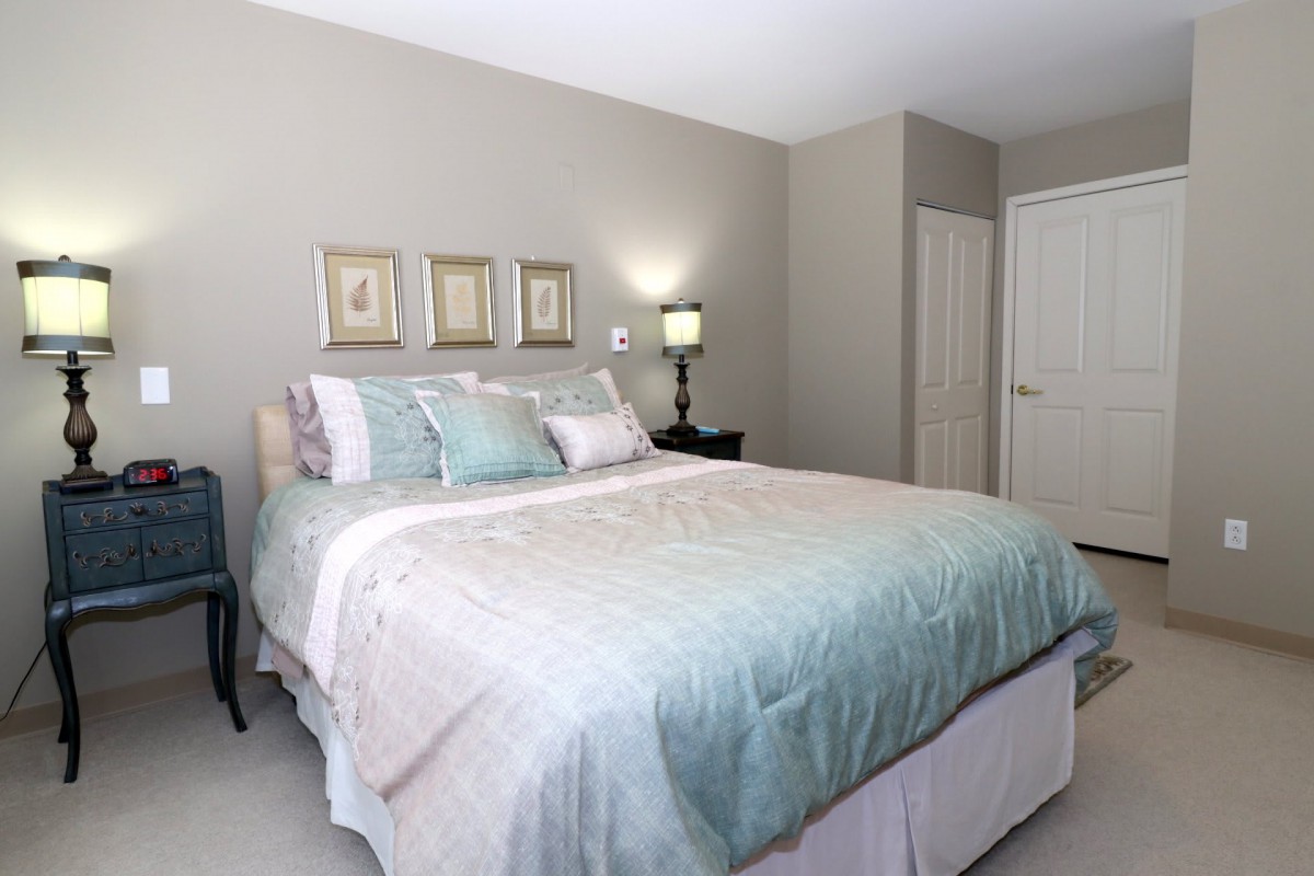 A cozy and well-decorated bedroom featuring a bed with pastel bedding, bedside lamp, and framed artwork on the wall.