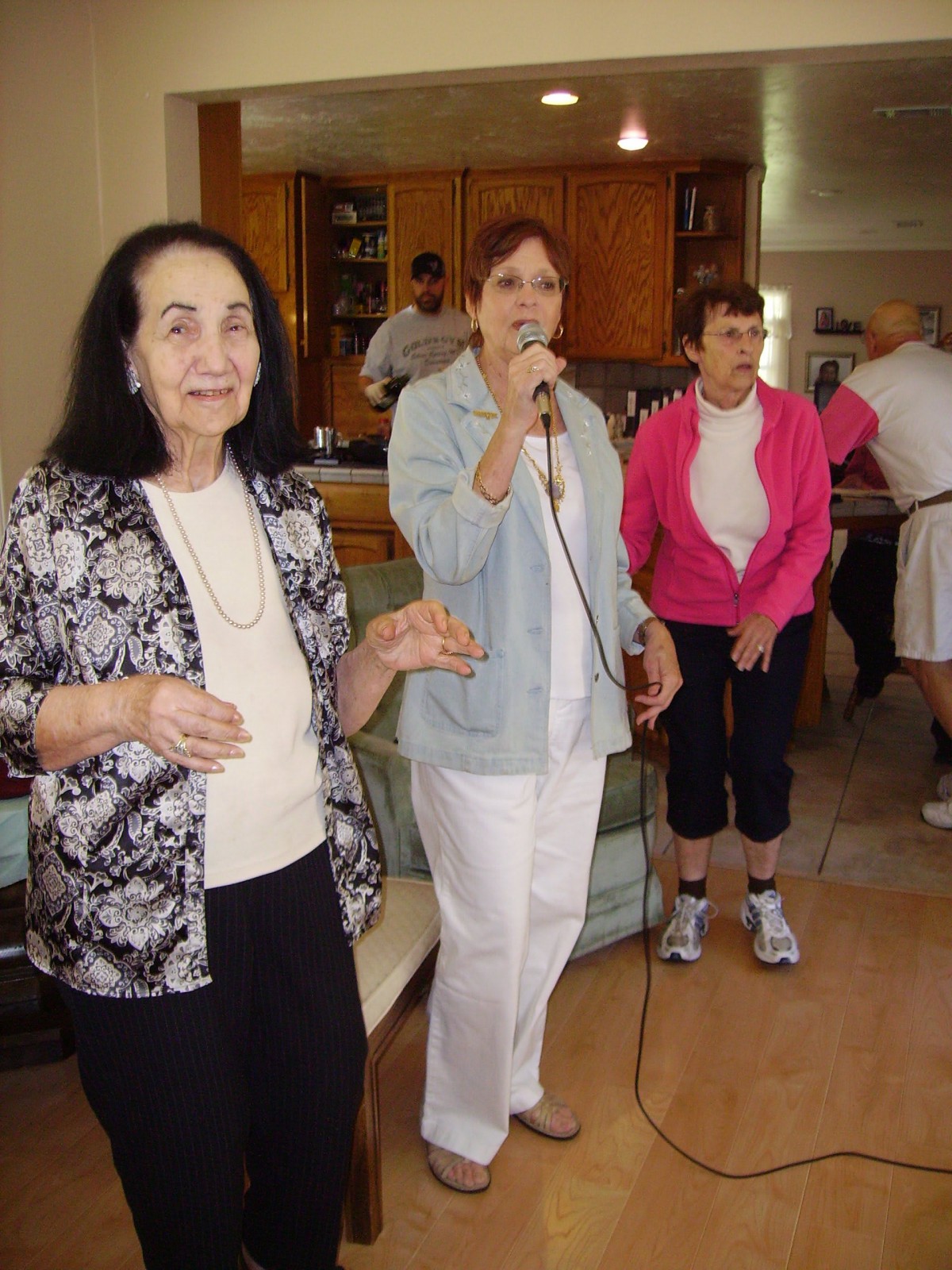 A group of people singing together indoors, one person holding a microphone.