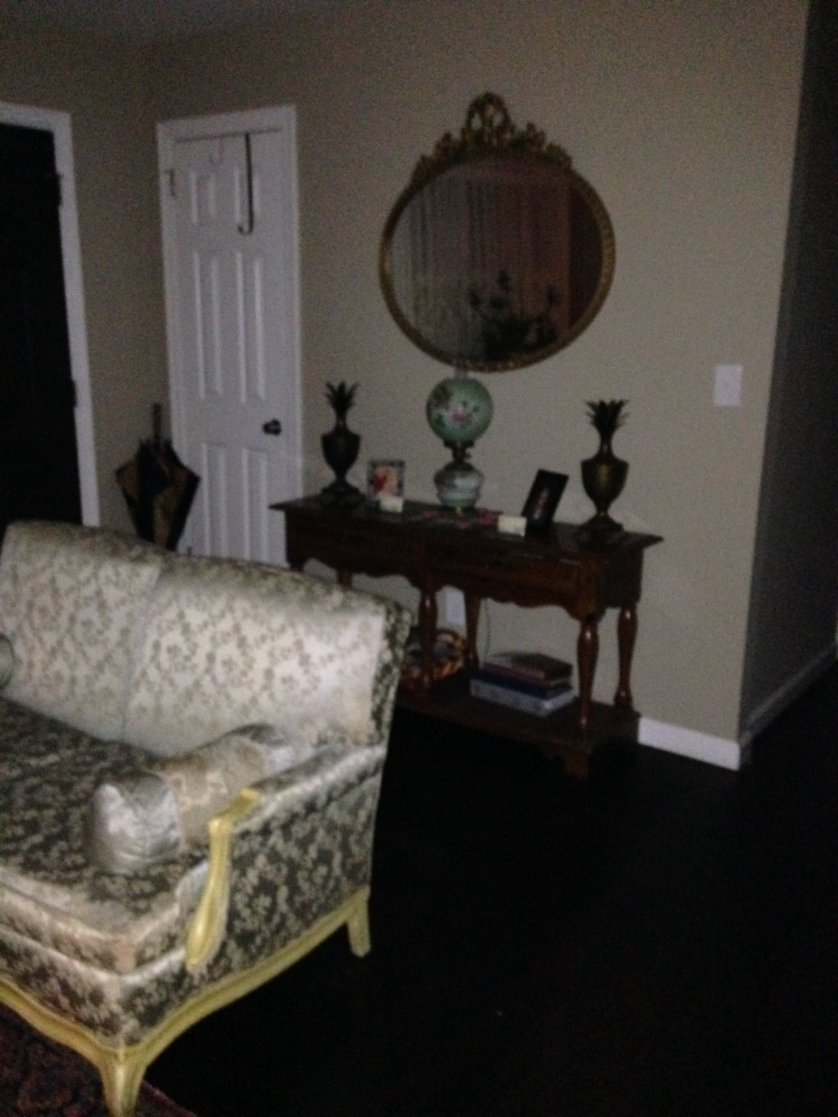 A cozy living room with an elegant sofa, a wooden table adorned with decor items, and a round mirror on the wall.