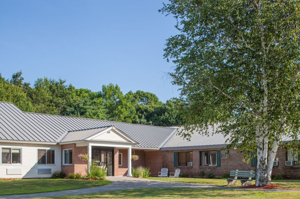 A single-story brick house with a well-maintained front yard and trees under a clear blue sky.