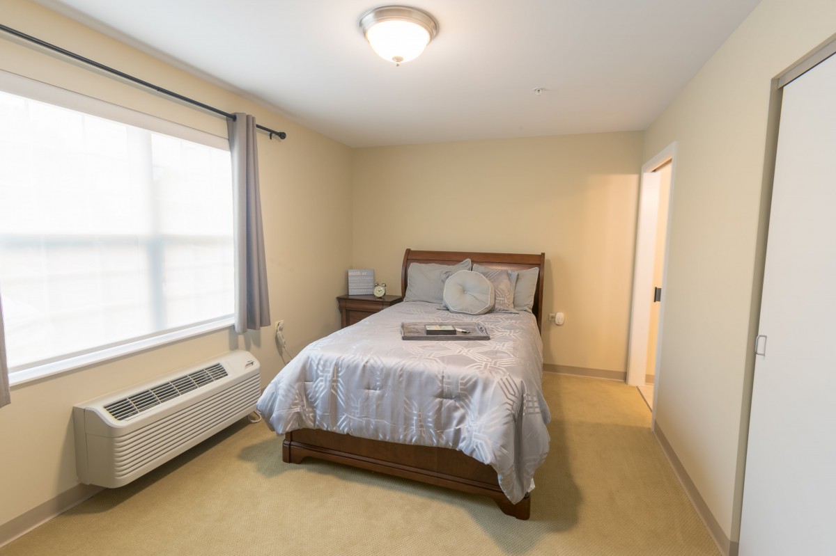 A cozy bedroom with a neatly made bed, soft lighting, and a window letting in natural light.