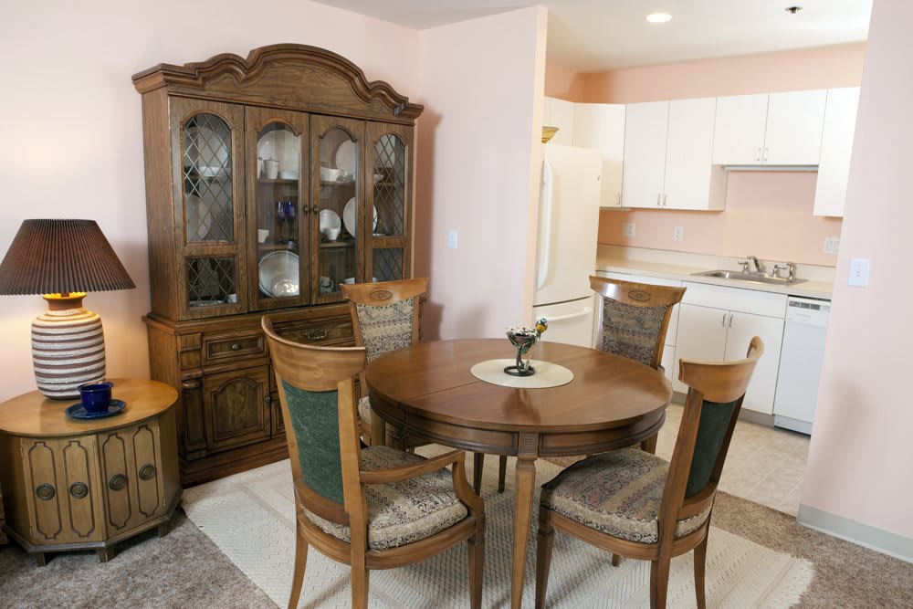 A cozy dining area with a wooden table, chairs, and a cabinet, adjacent to a kitchen.