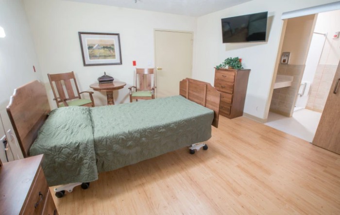 A simple bedroom with a single bed, television, and wooden furniture.