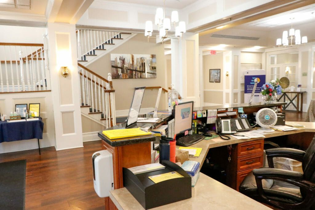 A modern office reception area with a desk, computer equipment, and a staircase in the background.