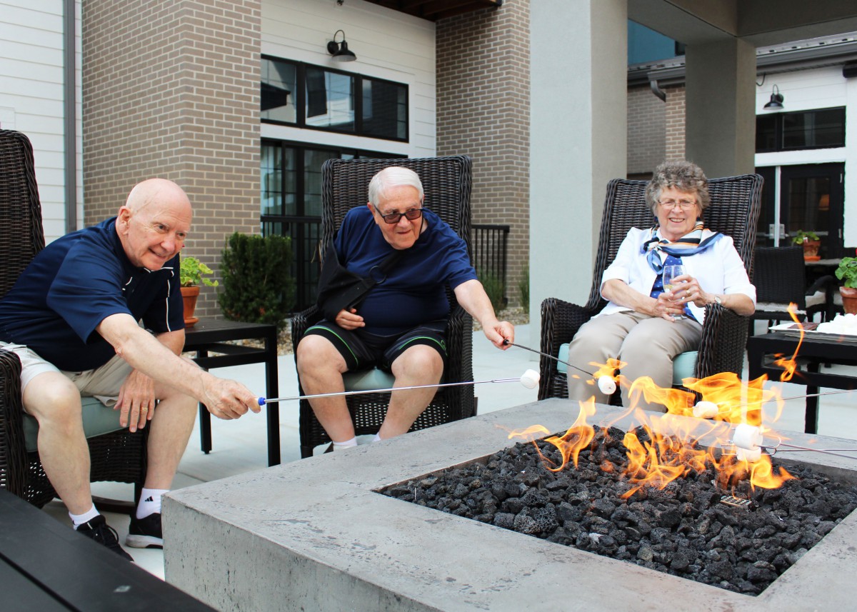 A group of seniors toasting marshmallows at an outdoor firepit.