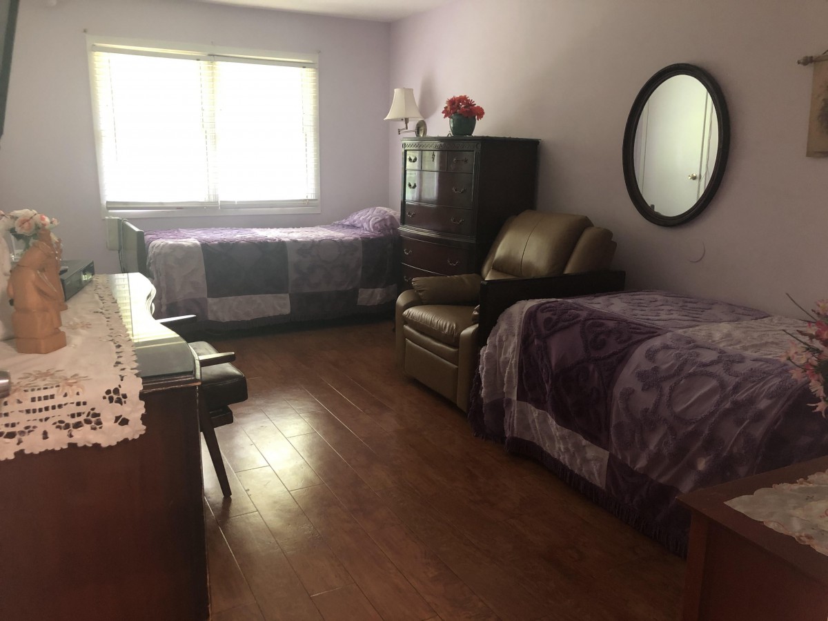 A cozy bedroom with two beds, purple blankets, a dresser, and a recliner.