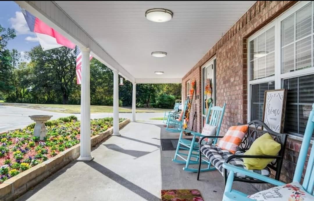 A cozy porch with rocking chairs and decorative pillows, next to a brick house and garden.