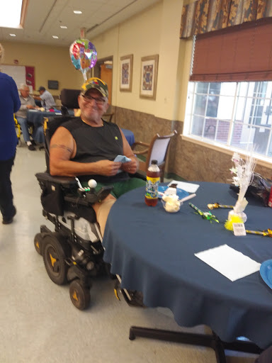 A man in a wheelchair sitting at a table in a community center, engaging in an activity.