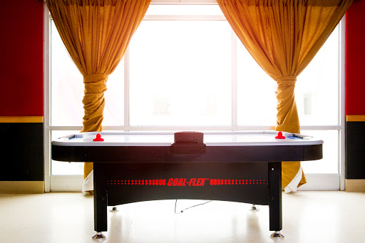 An air hockey table positioned in a well-lit game room, complemented by elegant curtains.
