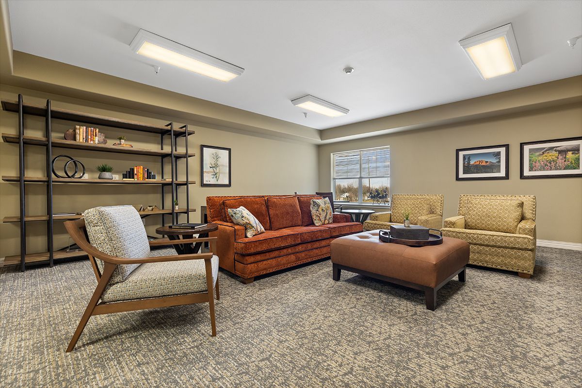A cozy living room with a mix of sofas and armchairs, featuring a central coffee table and a bookshelf.