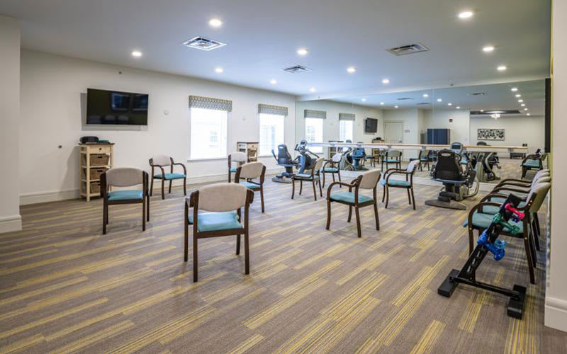 A spacious exercise room with chairs arranged in a circle and fitness equipment in the background.
