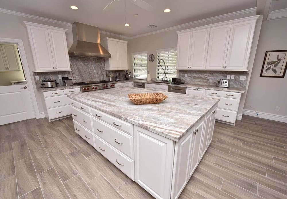 A spacious modern kitchen featuring white cabinets, a marble countertop island, and stainless steel appliances.