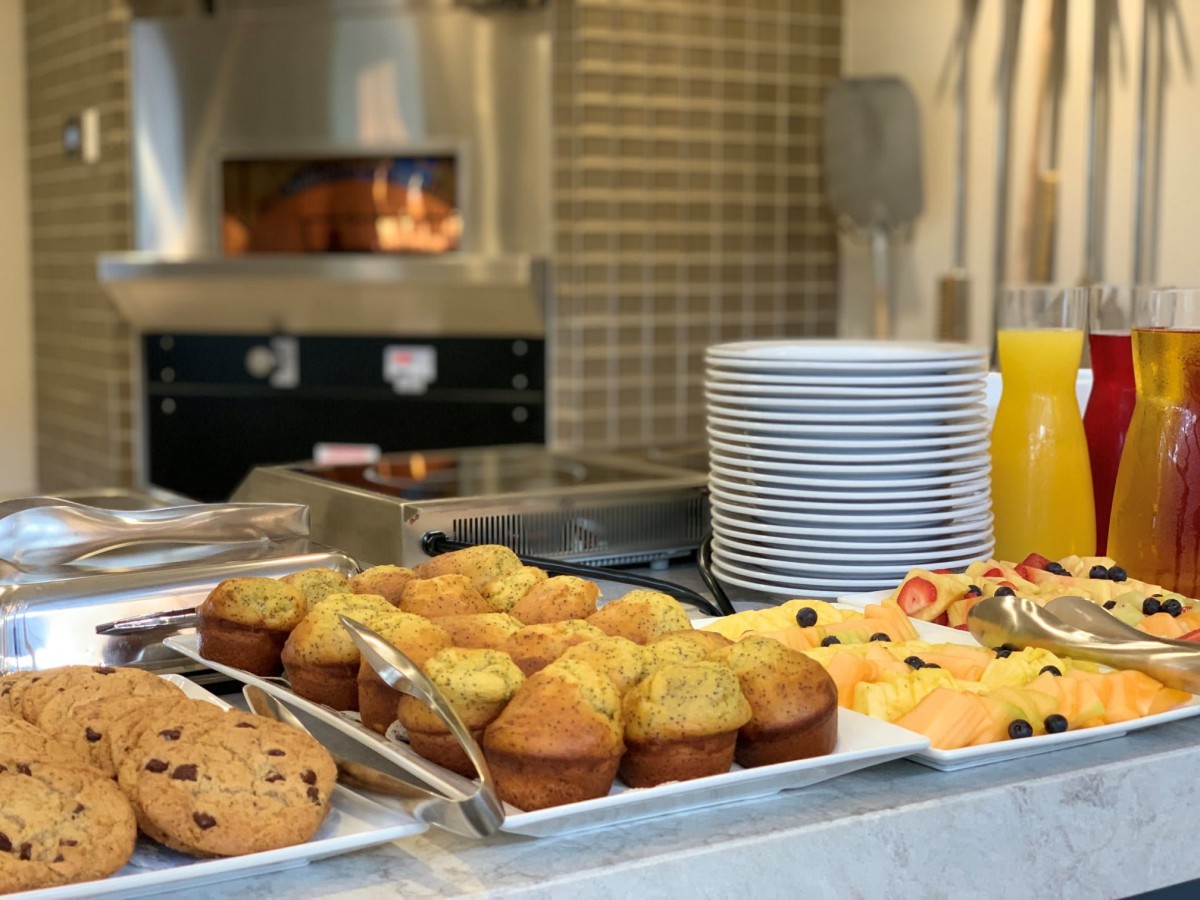 A breakfast buffet featuring muffins, cookies, fresh fruit, and orange juice.