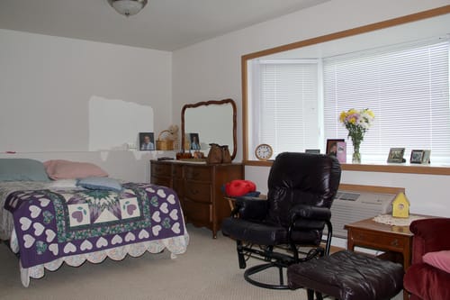 A cozy bedroom with a bed, dresser, and comfortable chair by the window.