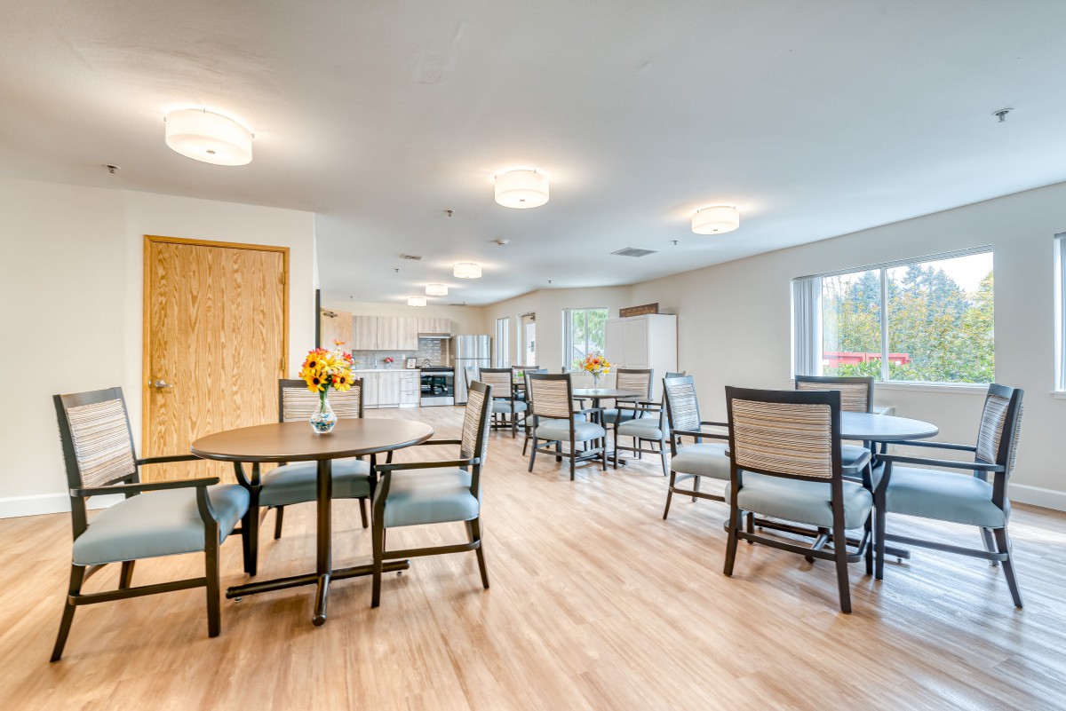 A modern dining area with several tables and chairs, featuring bright lighting and large windows.