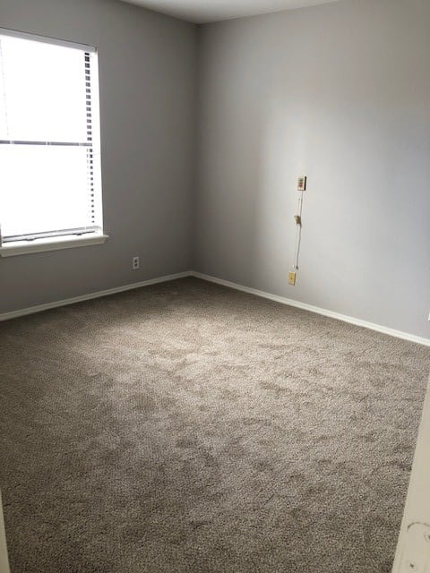 An empty room with a carpeted floor, a window, and neutral-colored walls.