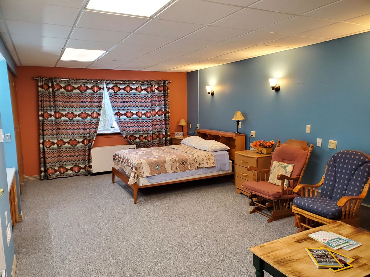 A cozy bedroom with a bed, chairs, and warm lighting.