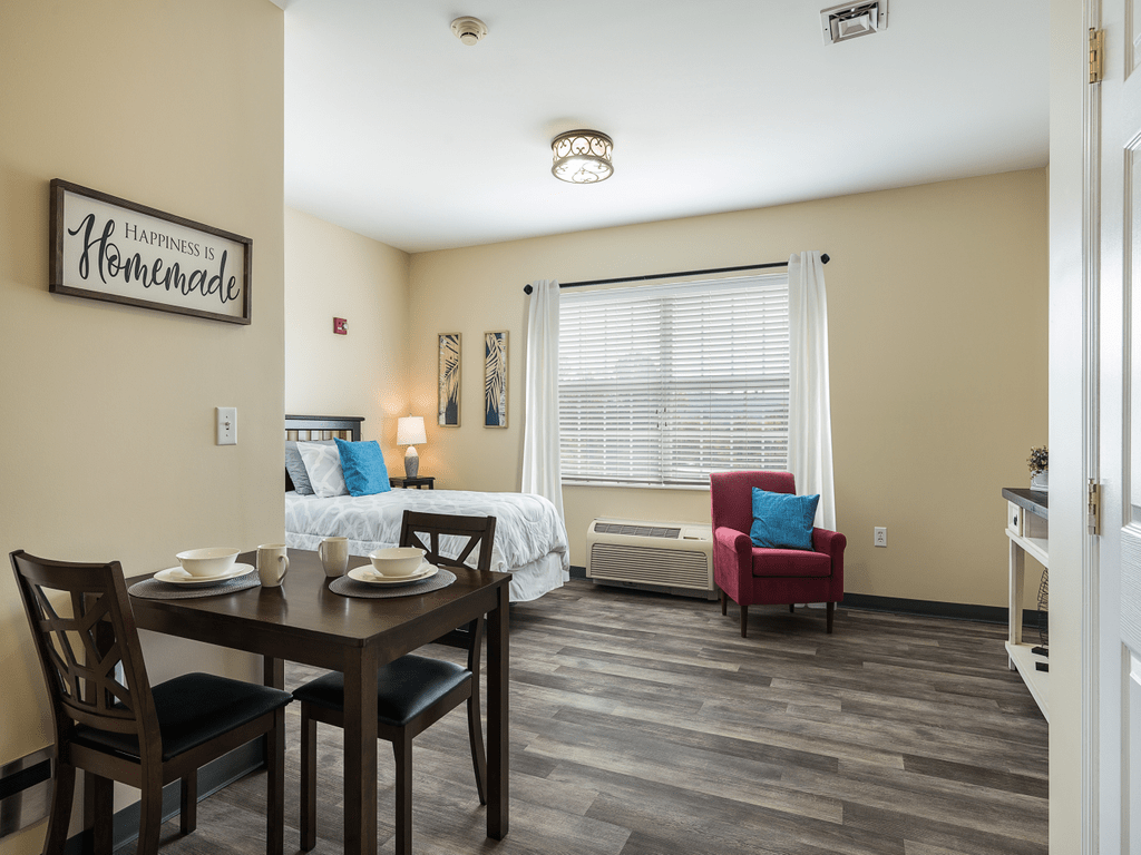 A cozy studio apartment with modern furnishings, featuring a bed, dining table, and a comfortable chair by the window.