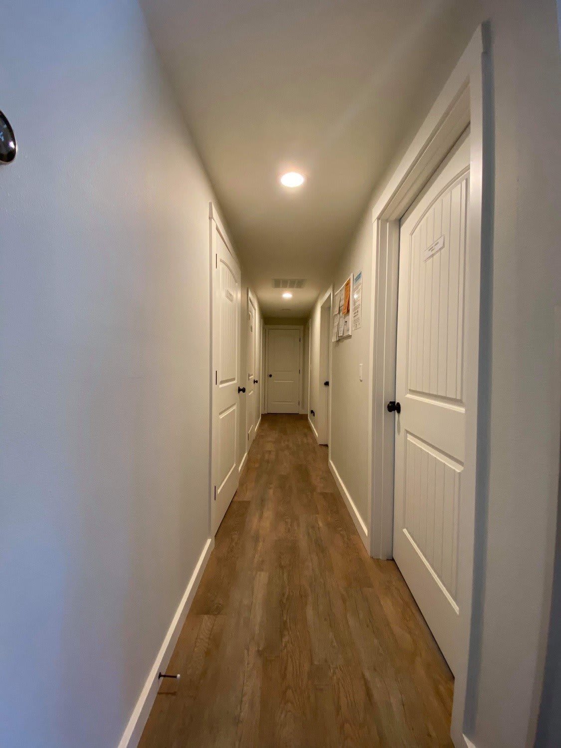A well-lit hallway with several doors and wooden flooring.