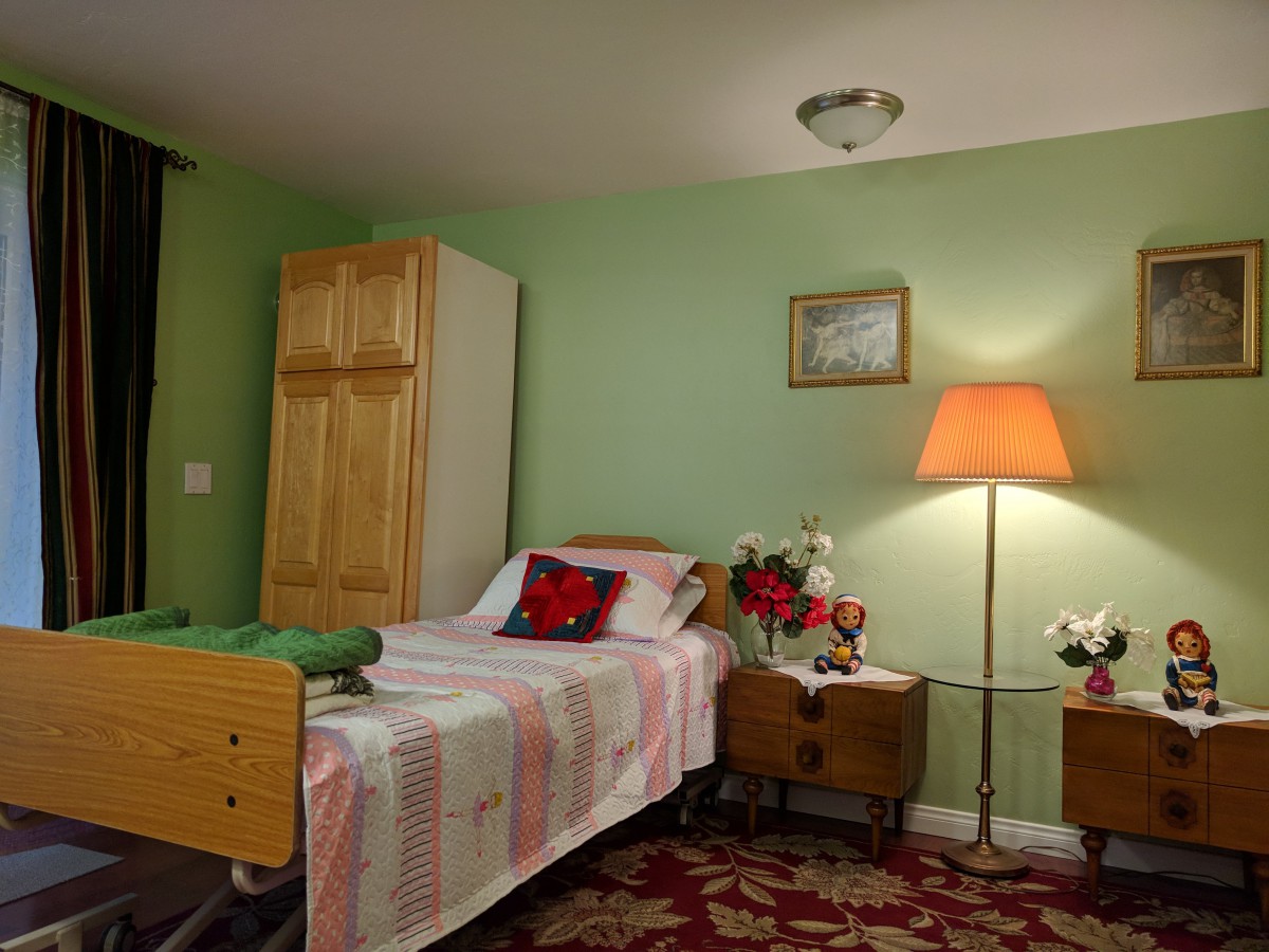 A cozy bedroom featuring a hospital bed, wooden furniture, a lamp, and decorative elements such as a vase with flowers.