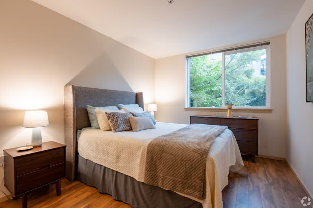 A cozy, modern bedroom with a neatly made bed, bedside lamps, and a large window.