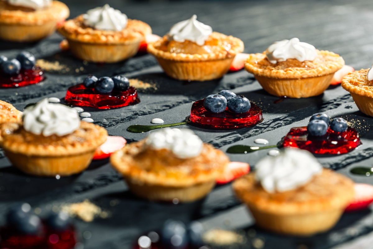Assorted tarts topped with whipped cream and garnished with berries on an elegant display.
