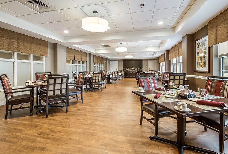 A spacious dining room with neatly arranged tables and chairs, featuring elegant lighting and a wooden floor.