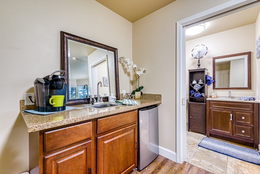 A cozy kitchen nook featuring a coffee maker, countertop with a mirror, and wooden cabinets.
