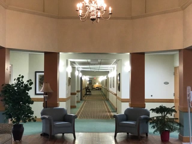 A well-lit lobby area featuring two chairs and a chandelier, leading into a long hallway.