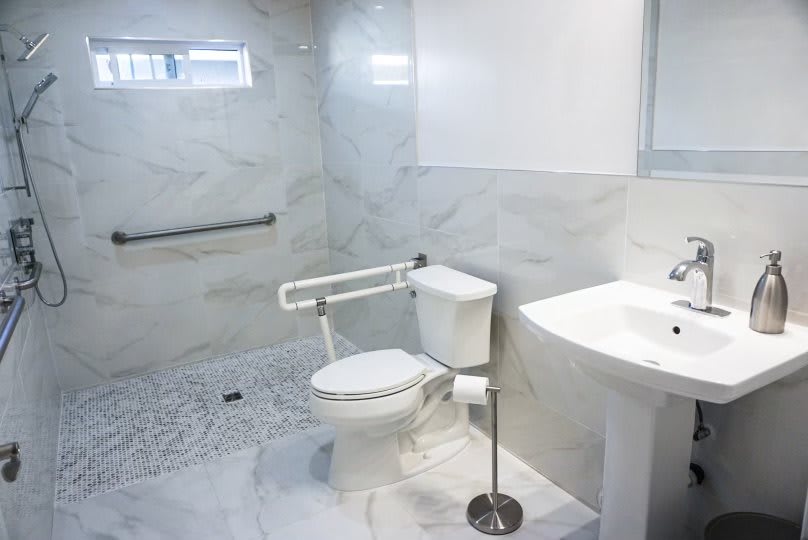 A modern and accessible bathroom with a grab bar, toilet, and sink.