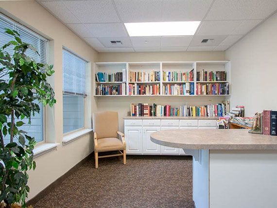A cozy reading area with a bookshelf filled with books, a comfortable chair, and natural light streaming through the windows.